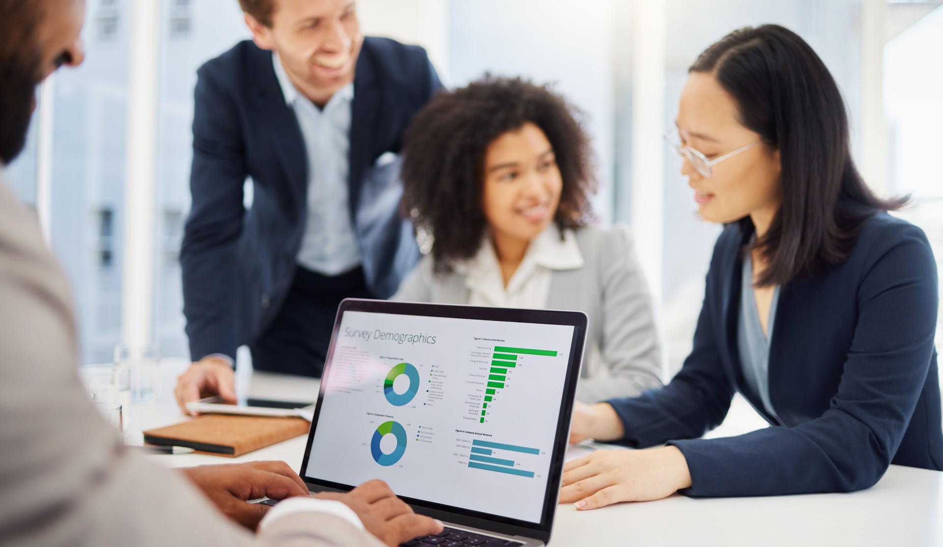 Closeup of a businessman analysing survey demographics from digital stats and data on a laptop in an office with his colleagues in the background. Entrepreneur reviewing infographics to present to his team